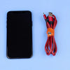 A black smartphone next to a bundle of red and black faux leather data cables and earphones.