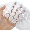 A hand holds a sheet of white self-adhesive hook and loop fasteners with circular pads.