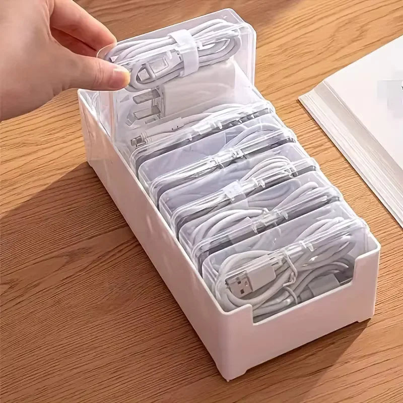 A hand is holding an open white plastic storage box filled with coiled white cables for organization.