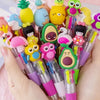 A hand holds a cluster of cute cartoon mini ballpoint pens in various bright colors like yellow, green, pink, and purple.