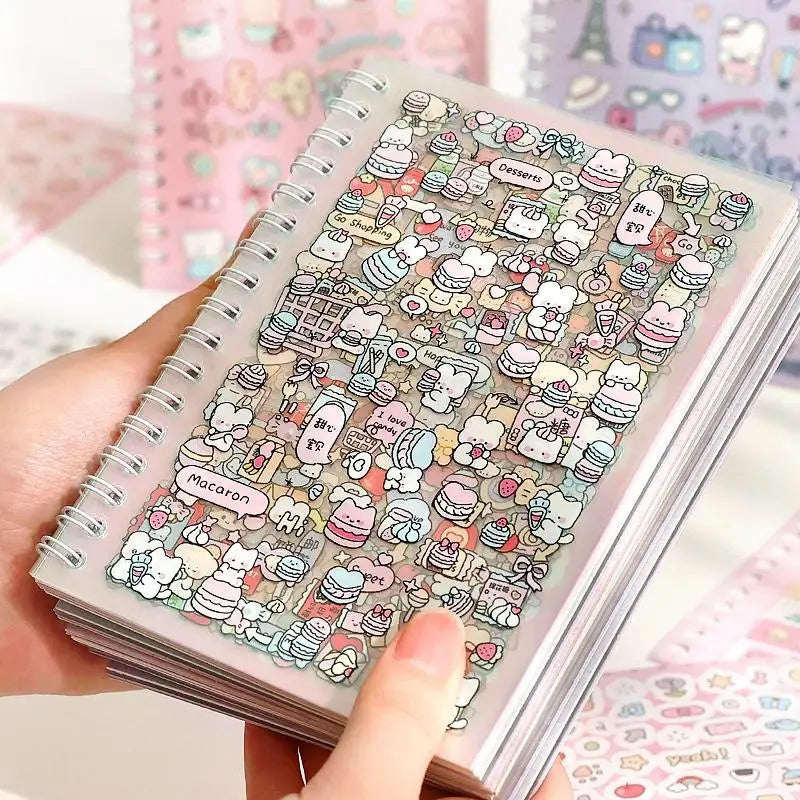 A hand holds a spiral-bound sticker book filled with cute cartoon stickers of desserts and food for scrapbooking