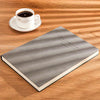 A gray notebook lies on a wooden surface next to a white cup of coffee.