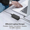 A close-up of a black 65W USB-C laptop charger plugged into a white laptop on a marble surface.