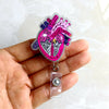 A hand holds a pink and purple anatomical heart diagram badge reel with a silver clasp.