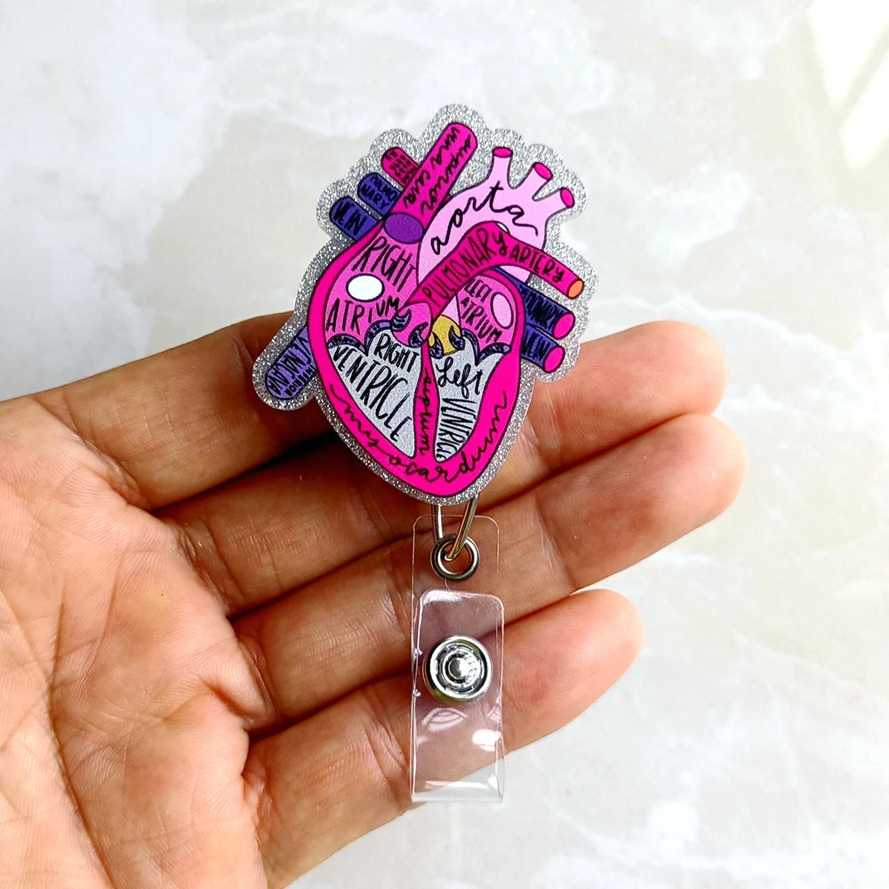 A hand holds a pink and purple anatomical heart diagram badge reel with a silver clasp.