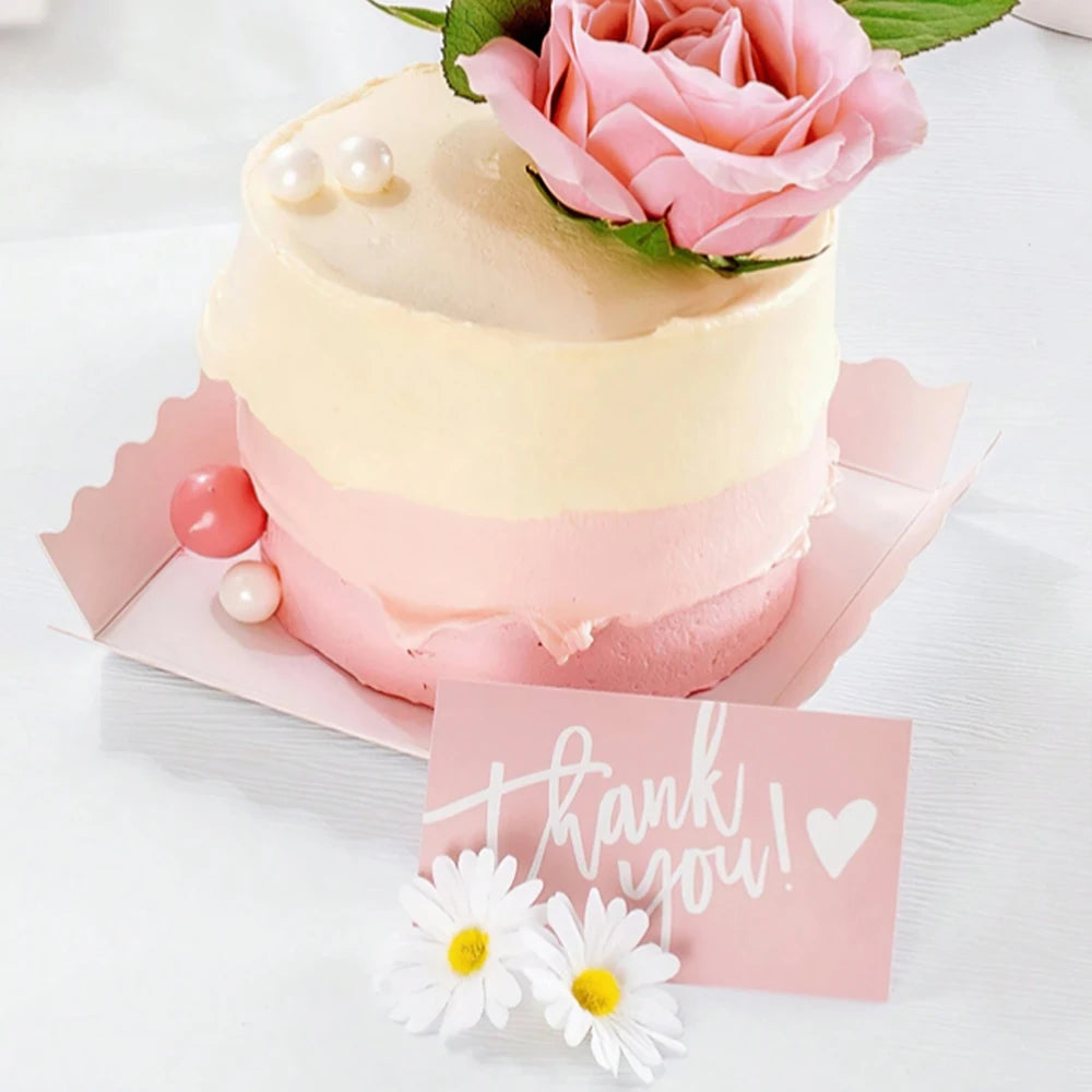 A pink and cream layered cake decorated with roses and pearl accents, presented on a pink card.