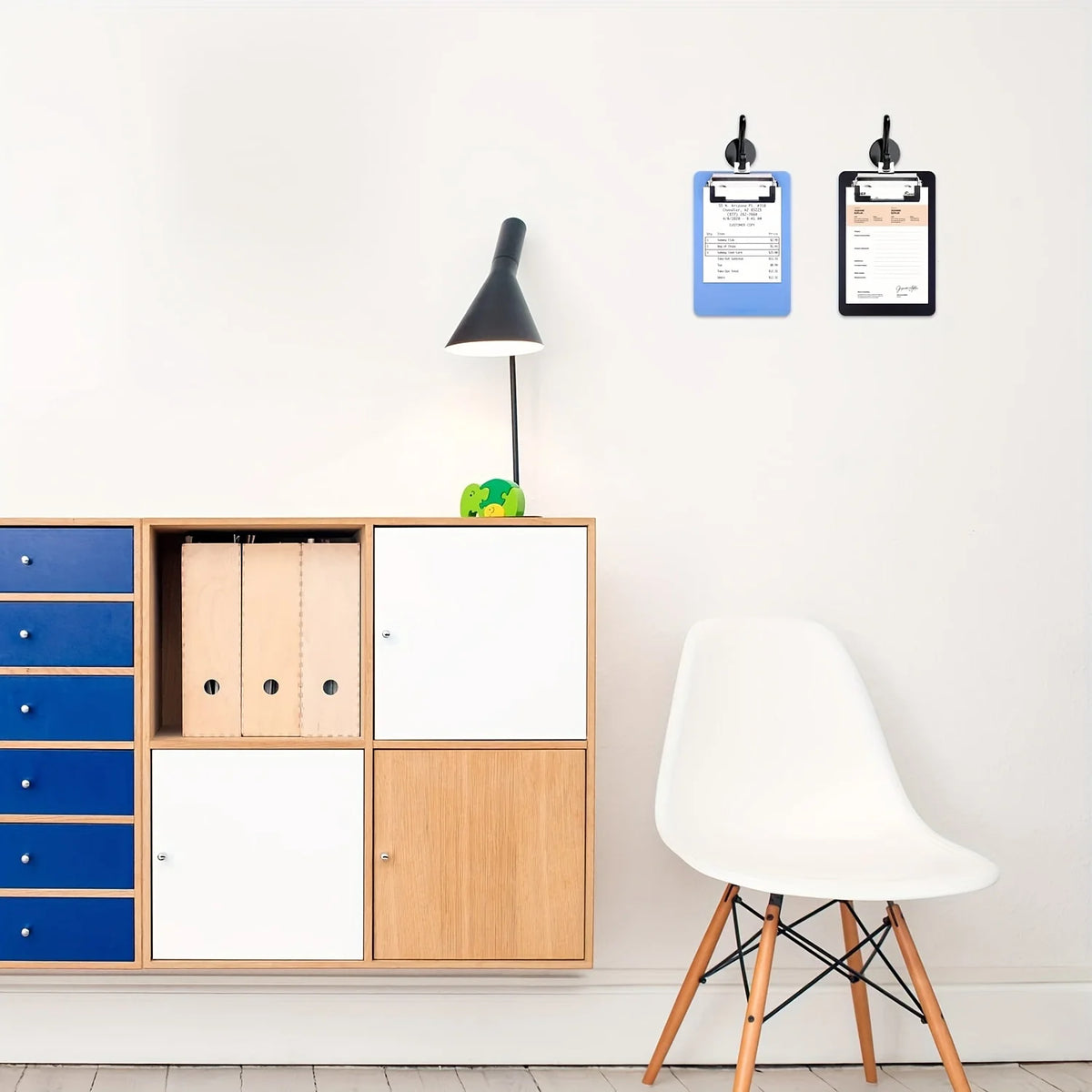 A white modern chair is positioned next to a wooden cabinet featuring storage compartments and two clipboards on the wall.