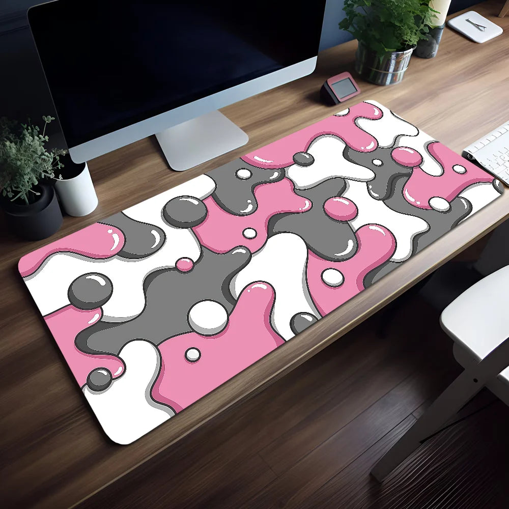 Pink and gray abstract wave pattern mouse pad placed on a wooden desk next to a computer monitor.