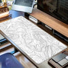 A black and white topographic map extended gaming mouse pad is displayed on a wooden desk next to a laptop.