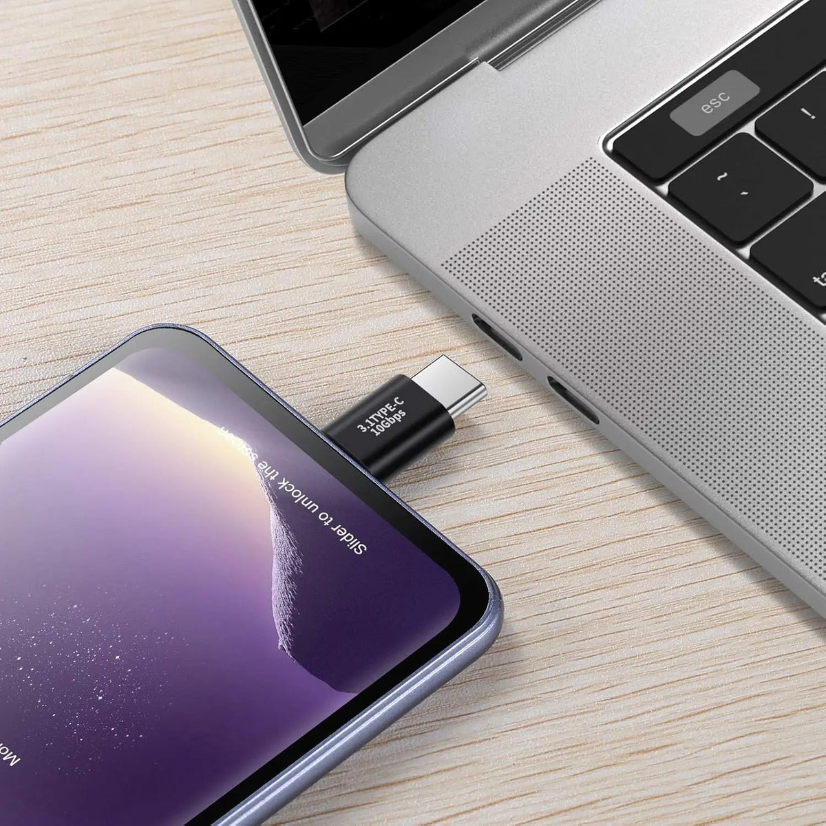 A close-up of a silver laptop next to a purple smartphone with a USB-C adapter plugged in.