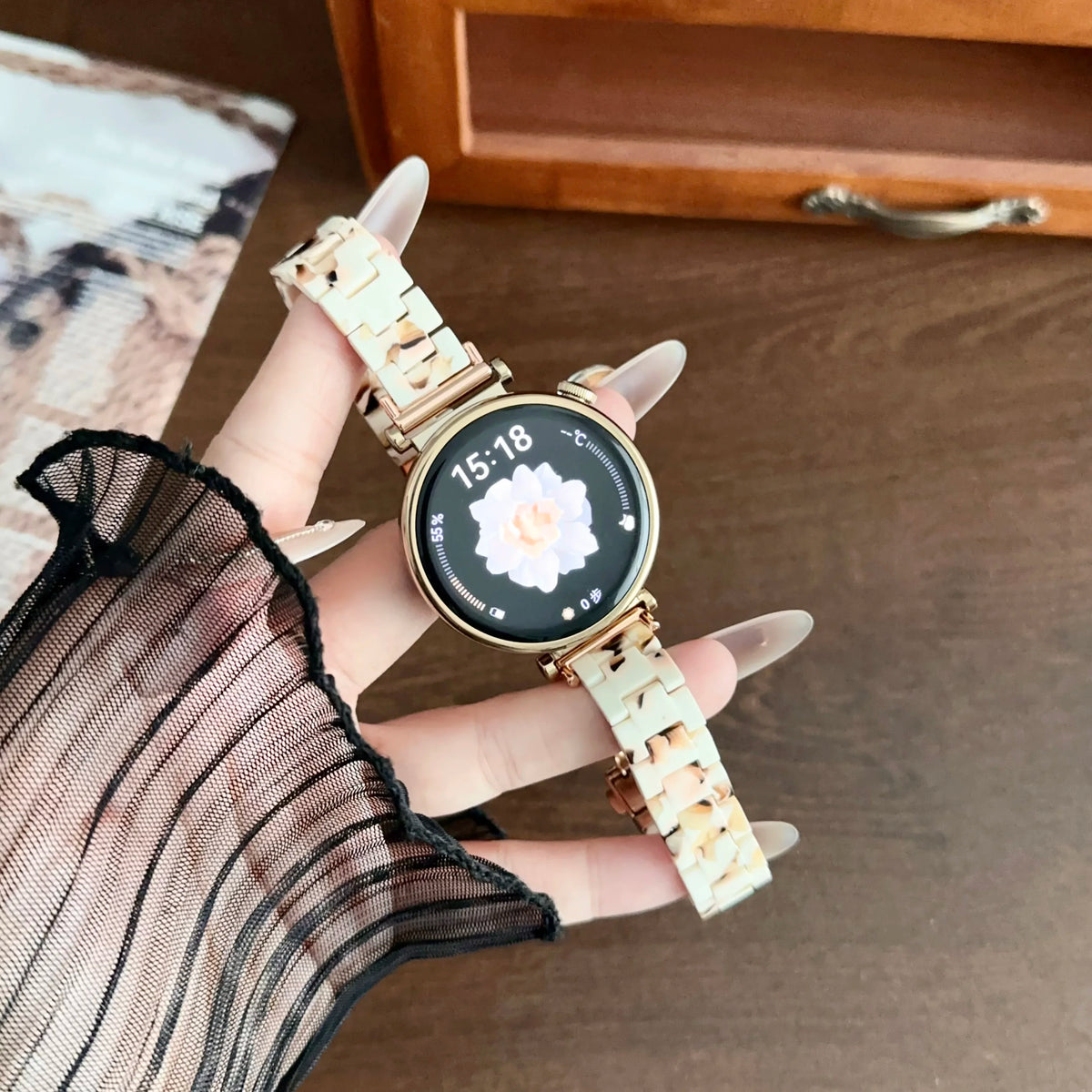 A hand is holding a resin beaded watch with a light beige band and a round face displaying the time 15:18.
