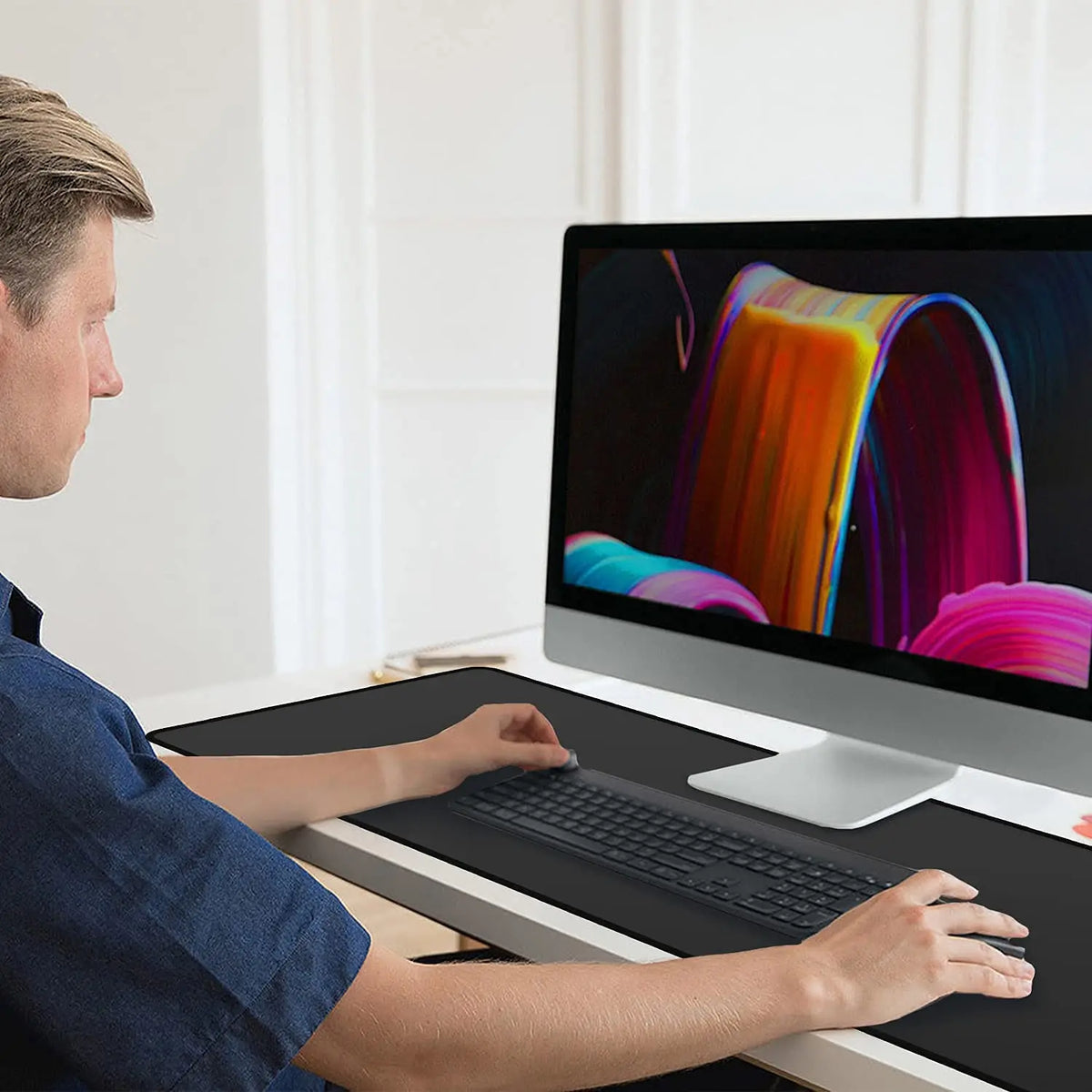 A man uses an extra large anti-slip rubber mouse pad on a desktop computer.