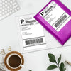 A purple thermal shipping label is shown on a white sheet, next to a laptop and a cup of coffee.
