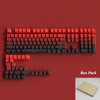 Paquete de keycaps PBT rojas y negras con retroiluminación RGB sobre una superficie roja.