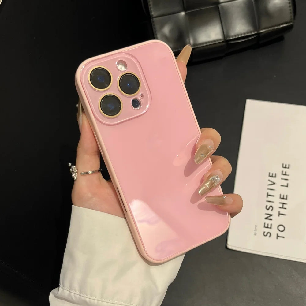 A hand holds a pink iPhone with a clear case and gold-accented nails against a dark background.
