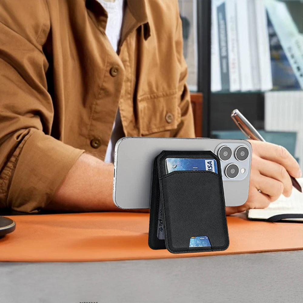 Une main tient une pochette de portefeuille en cuir magnétique noir pour iPhone sur un bureau en bois.