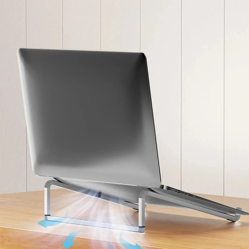 A silver foldable aluminum laptop stand is shown resting on a wooden surface, demonstrating its non-slip grip.