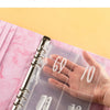 A hand holds a transparent inner page of an A5 marble budget binder showing cash envelopes.