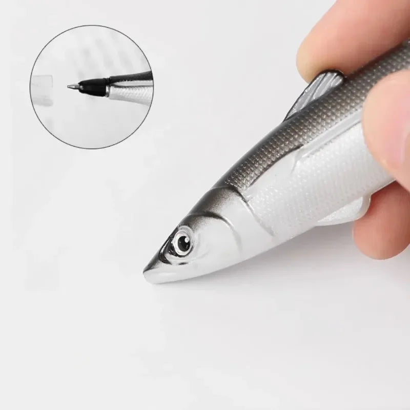 A hand holds a silver ocean fish ballpoint pen, showing a close-up view of the tip.