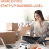 A woman is using a phone while sitting on a couch with several cardboard boxes and a laptop in the background.