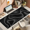 A black and gray abstract art desk mat with a non-slip rubber base is displayed on a white desk next to a laptop.