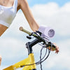 A person is using a purple USB clip-on cooling fan attached to a bicycle handlebar outdoors.