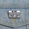 Silver enamel pin with text 'In My Defense I Was Left Unsupervised' pinned on denim fabric.