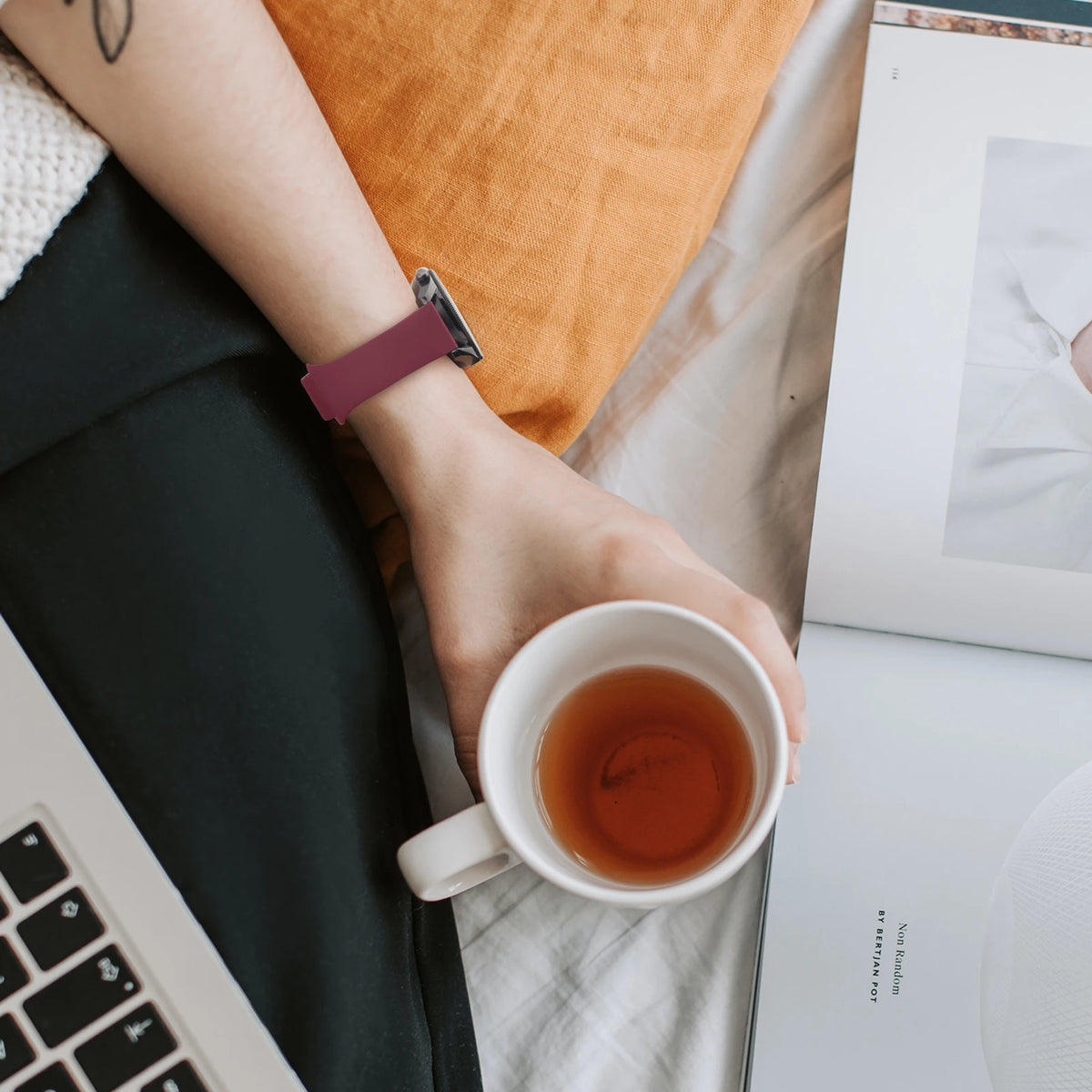 Eine Hand mit einem lila Silikon-Schnellverschluss-Armband hält eine Tasse Tee neben einem Laptop.