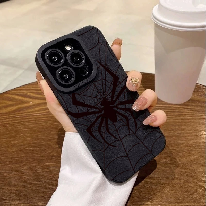 A hand holds a black phone case featuring a spider web design, next to a white cup.