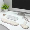 Un ensemble de trois repose-poignets en forme de nuage blanc sur un bureau, à côté d'un écran et d'une plante verte.