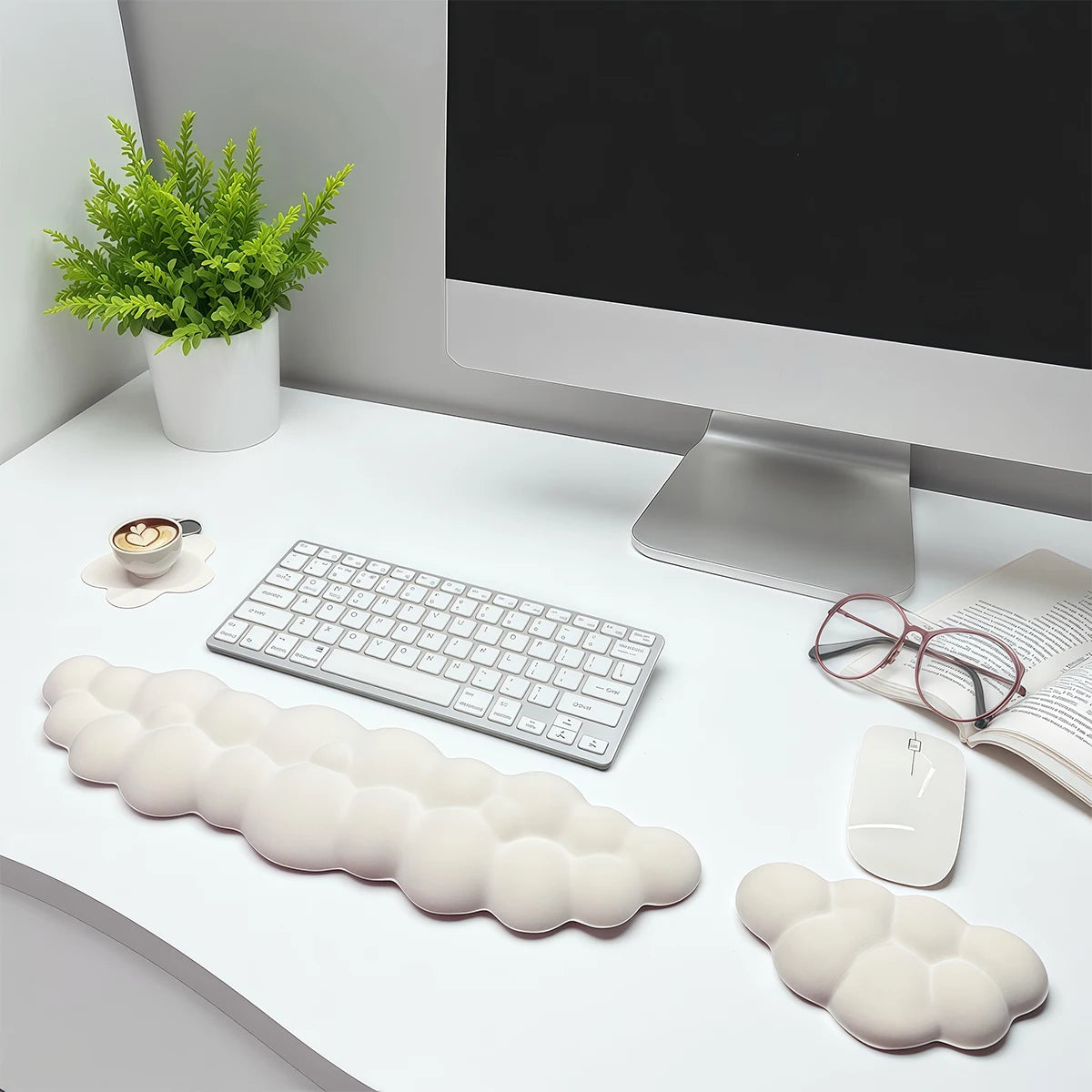 Un ensemble de trois repose-poignets en forme de nuage blanc sur un bureau, à côté d'un écran et d'une plante verte.