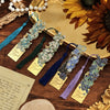 A collection of vintage artistic metal bookmarks with tassels in various shades of blue and green resting on a wooden surface