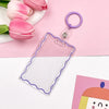 Clear acrylic card holder with a purple keychain attached, resting on a pink background.