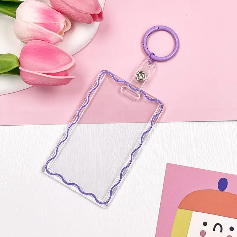 Clear acrylic card holder with a purple keychain attached, resting on a pink background.