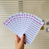 A hand holds a stack of A6 budget planner sheets with envelope pockets and expense sheets against a light wood background.