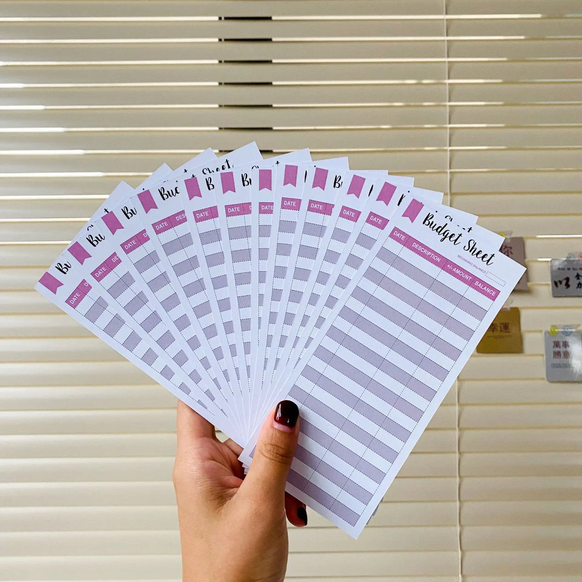 A hand holds a stack of A6 budget planner sheets with envelope pockets and expense sheets against a light wood background.