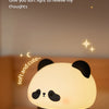 A white panda silicone night light with black accents sitting on a wooden surface.