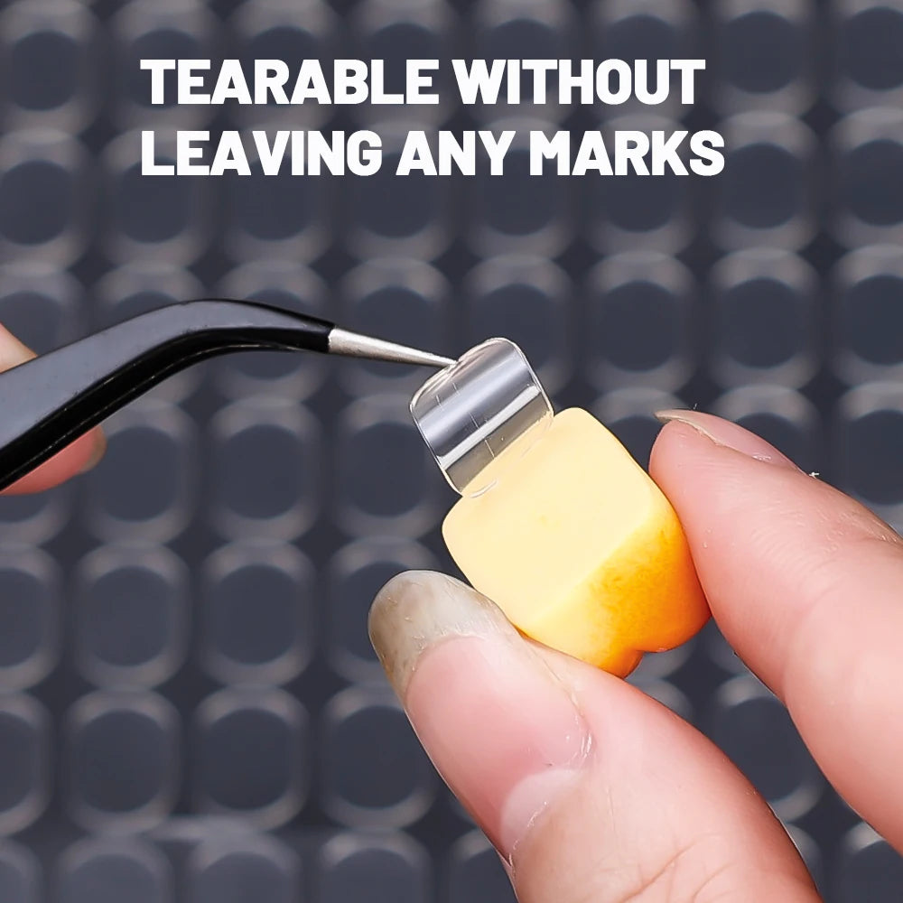 A hand is using a pair of tweezers to tear off a yellow adhesive fixer pad from a black tool.