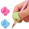 A hand holds a pink silicone pencil grip writing corrector, showing the grip and the pencil tip.