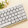 A close-up view of a white mechanical keyboard with light-colored keycaps and a sprig of white flowers.
