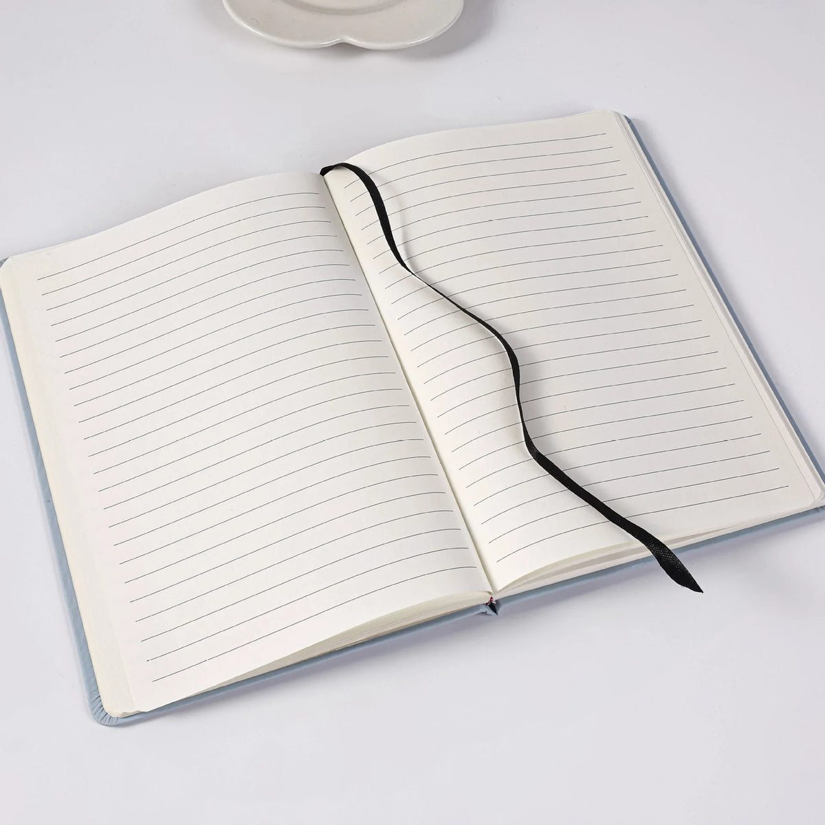 An open A5 lined notebook with black binding lies on a white surface.