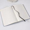 An open A5 lined notebook with black binding lies on a white surface.