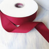 Roll of matte finish satin ribbon in deep magenta color unwrapped and laid on a white surface.