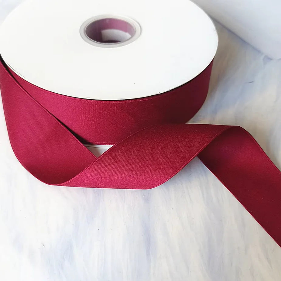 Roll of matte finish satin ribbon in deep magenta color unwrapped and laid on a white surface.