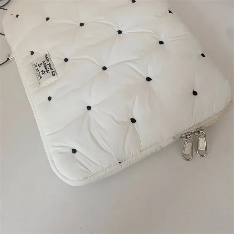 A white padded laptop sleeve case with quilted texture and a small tag is shown on a light surface.