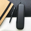 A black compact EVA hard shell pencil case with a zipper and mesh pockets resting on a white surface next to a black pen.