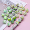 A collection of handmade acrylic flower beads in various shades of green and yellow are displayed on a white card.