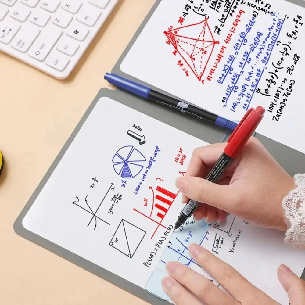 A hand is writing on a whiteboard with various mathematical formulas and diagrams, next to a laptop and a pen.