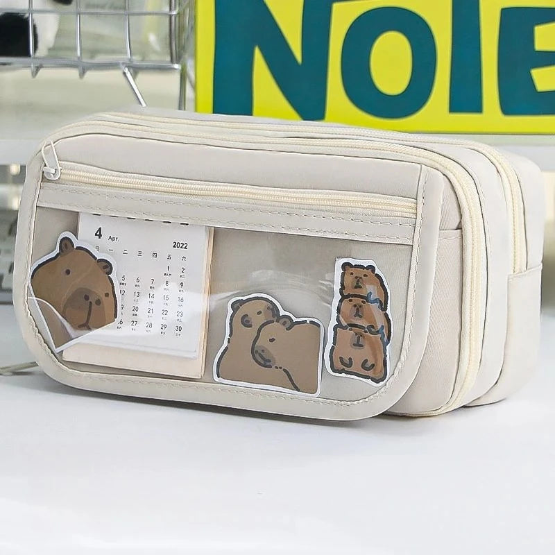 A beige pencil case with a transparent flip pocket featuring bear illustrations and a calendar.