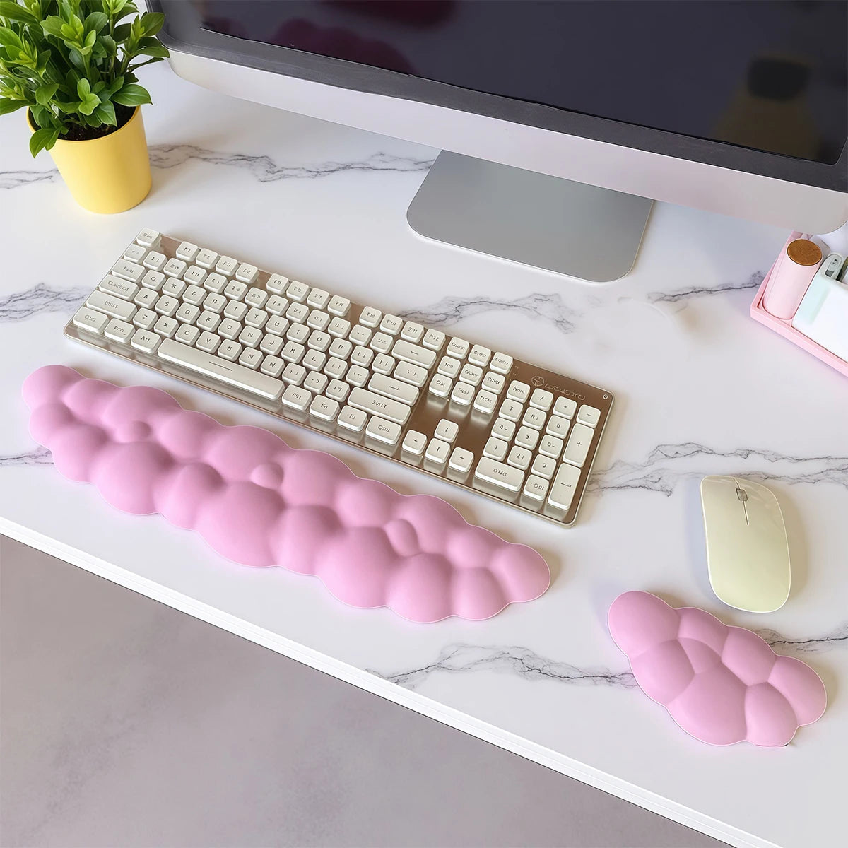 A pink memory foam wrist rest pad is placed on a white desk next to a silver keyboard and mouse.